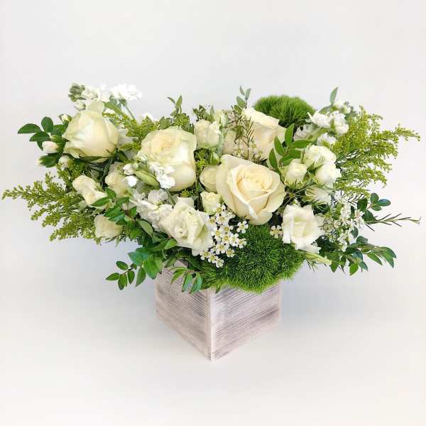 White roses and small white flowers in a square vase with green accents