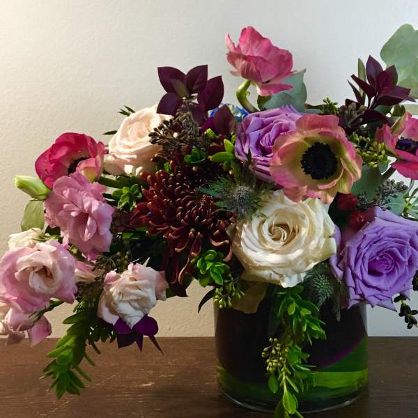 Mixed bouquet of roses, poppies, and chrysanthemums in a glass vase