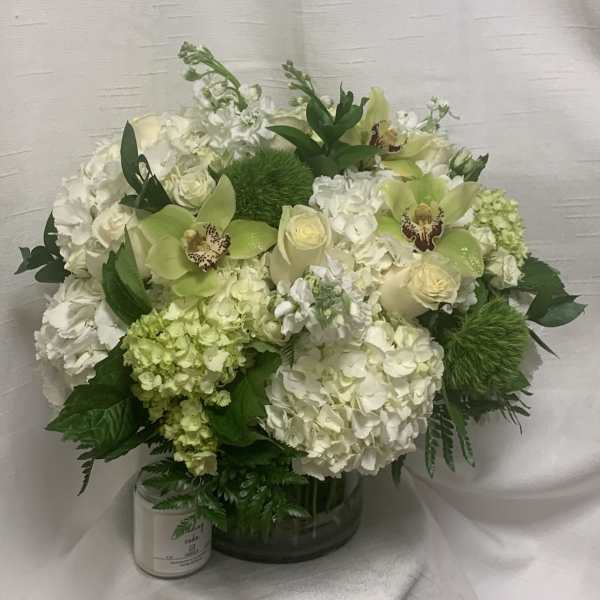 Round arrangement of white hydrangeas, cream roses, and green orchids in a clear glass vase
