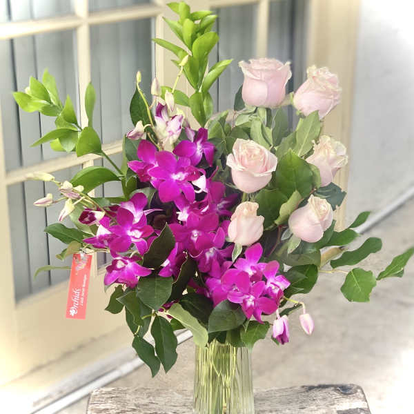 Pink roses and purple orchids in a clear glass vase