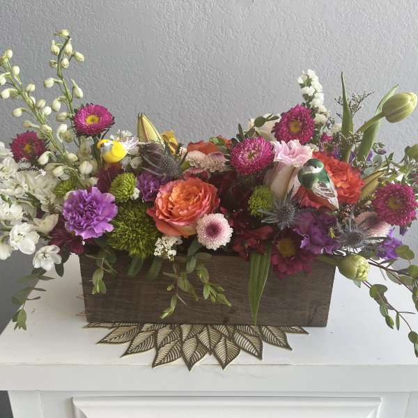 Mixed floral arrangement in a wooden box with pink, orange, white, and purple blooms