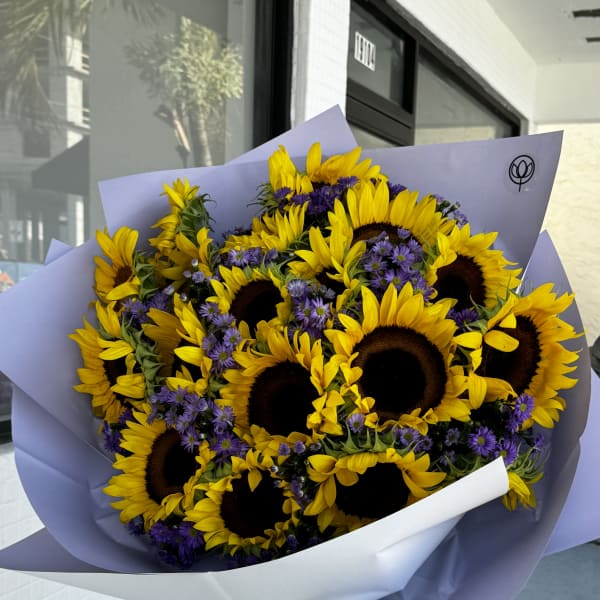Bouquet of sunflowers and purple daisies wrapped in lavender paper