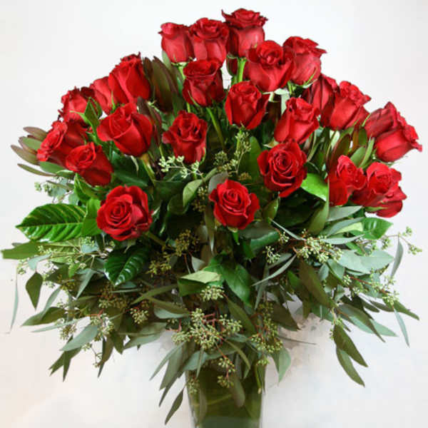 Red roses arranged in a clear glass vase with greenery