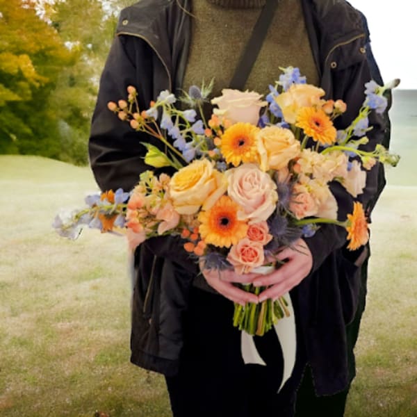 Person holding a bouquet of peach, pink, and orange flowers