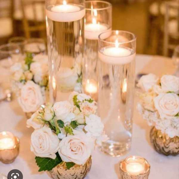 White rose centerpieces with tall glass candles on a table