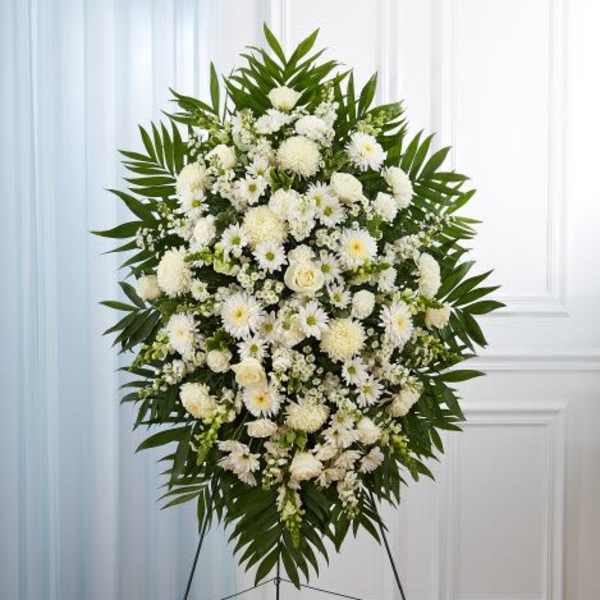 Standing spray of white roses, daisies, and mums with palm fronds on a metal easel.