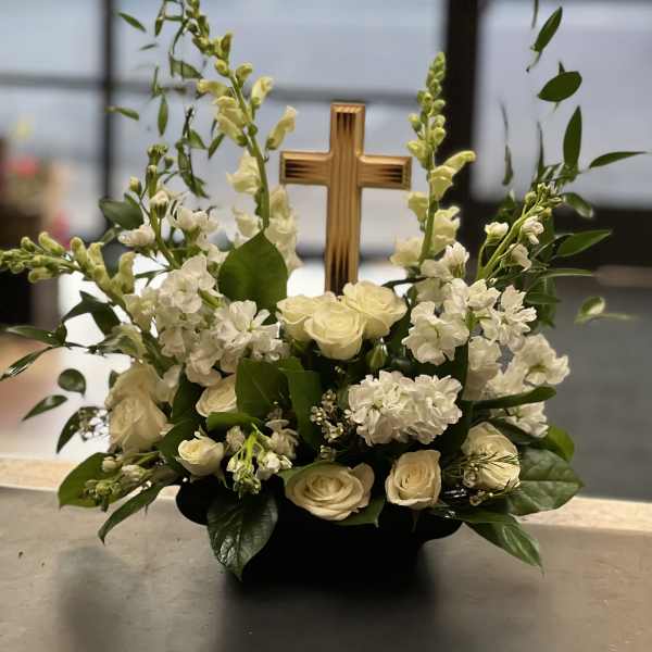 White roses and snapdragons arranged around a wooden cross