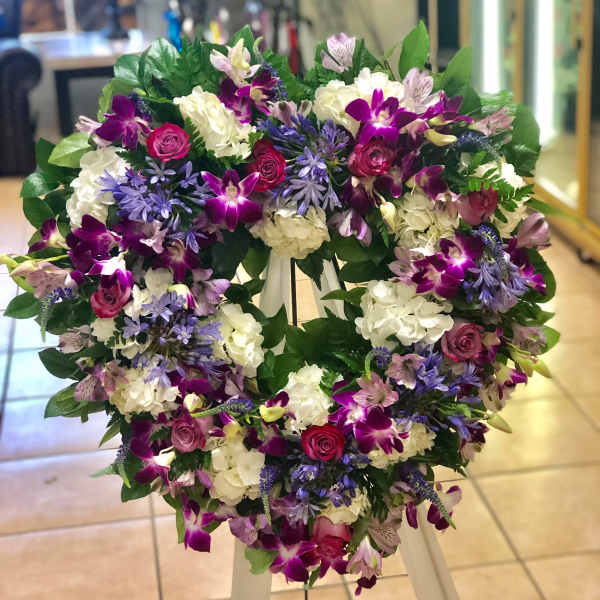 Heart-shaped standing wreath with purple orchids, pink roses, and white hydrangeas on a white easel