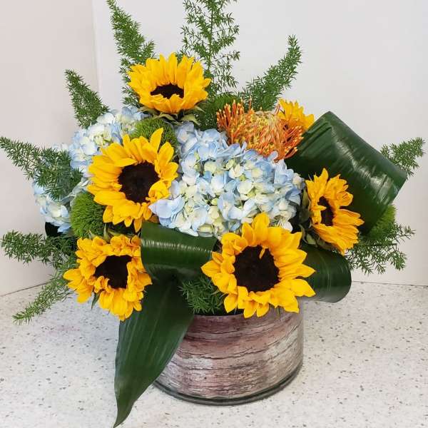 Sunflowers and blue hydrangeas in a rustic container