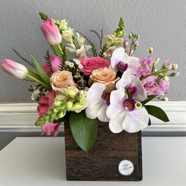Mixed bouquet in a wooden box with pink tulips, roses, and white orchids