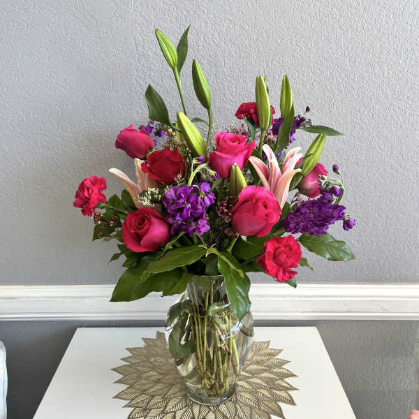 Mixed bouquet of pink roses, lilies, and purple flowers in a clear glass vase
