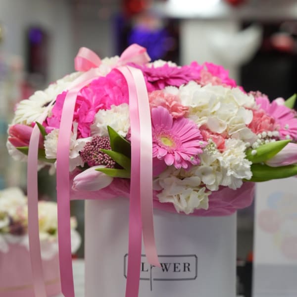 Pink and white flower arrangement in a white hatbox with ribbon