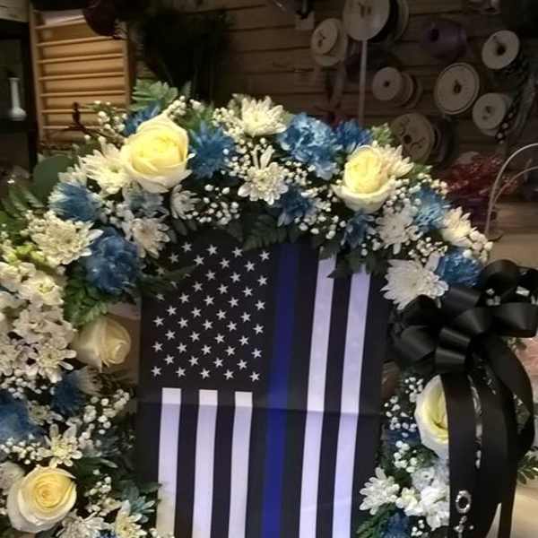 Floral wreath around a black-and-white flag display with yellow roses and blue flowers