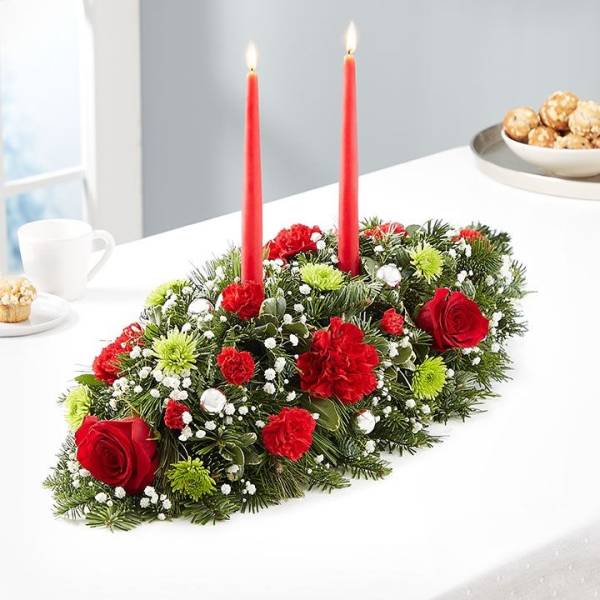 Holiday centerpiece with red candles and red flowers on evergreen
