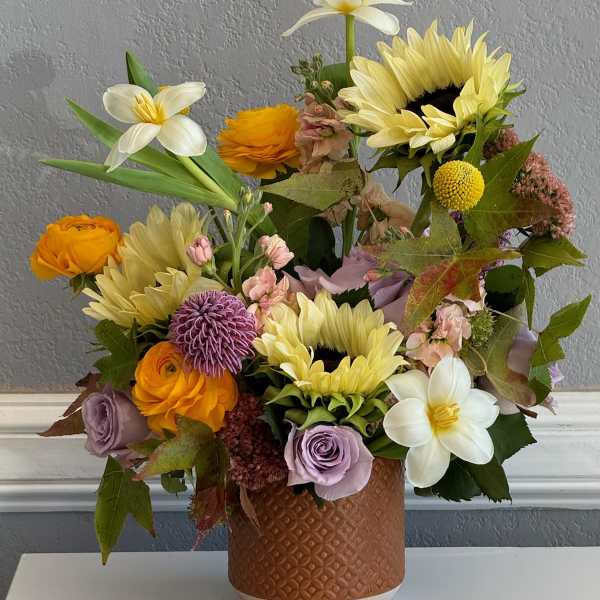Mixed bouquet of sunflowers, roses, and white daffodils in a textured vase
