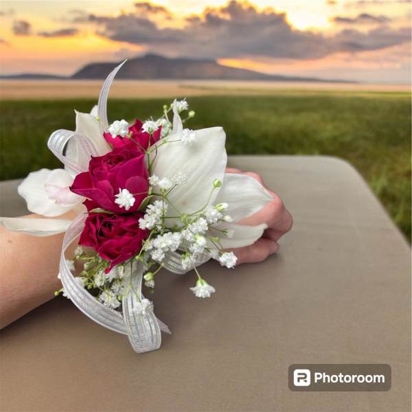 Small wrist corsage with pink roses and white petals tied with silver ribbon