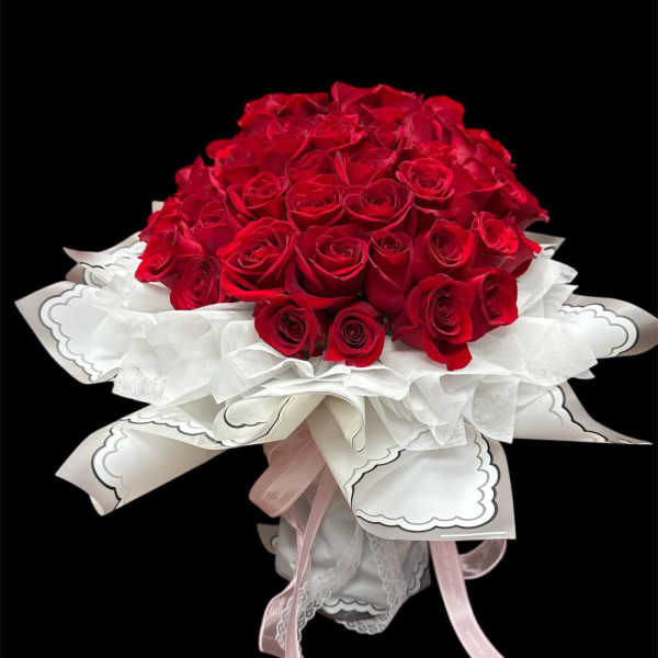 Bouquet of red roses wrapped in white paper with pink ribbons
