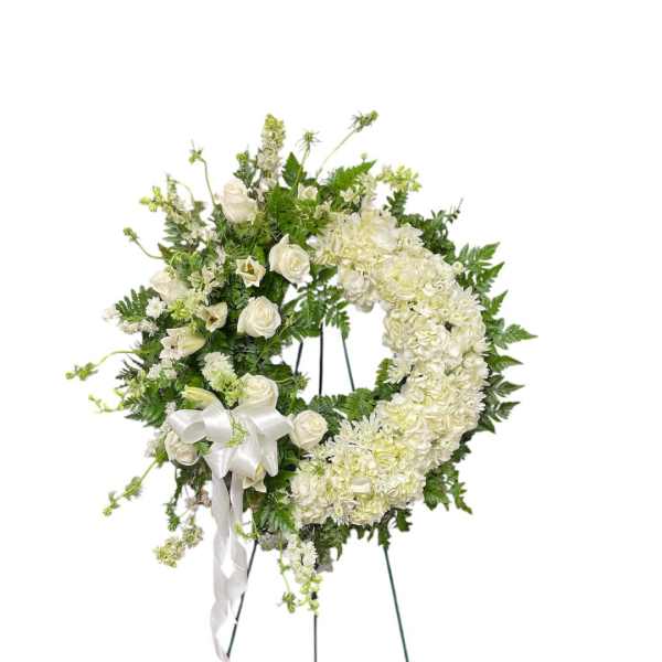 White floral wreath on a standing easel with a ribbon bow