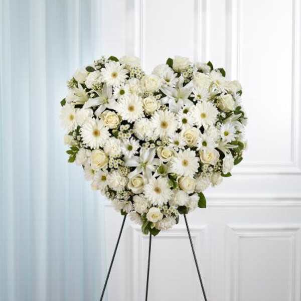 Heart-shaped standing spray of white roses, lilies, and mums on a tall metal easel
