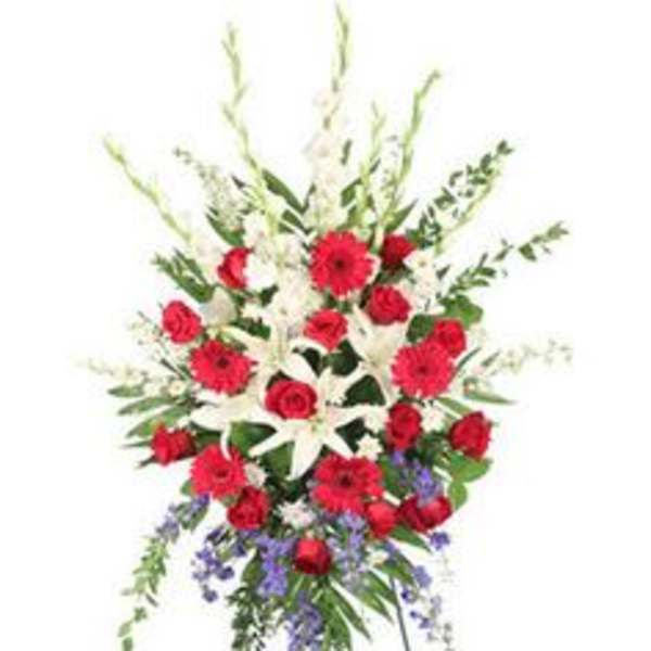 Tall standing spray of red roses and gerbera daisies with white lilies and purple accents on an easel.