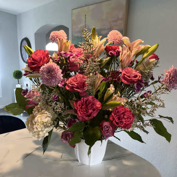 Large pink and peach floral arrangement in a white vase