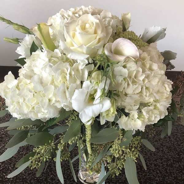 White floral arrangement with roses, hydrangeas, and calla lilies in a glass vase
