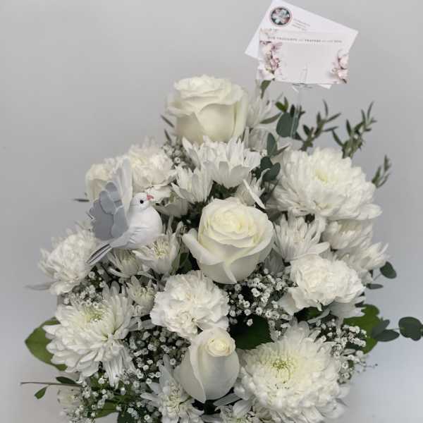 White floral arrangement in a clear vase with a small dove decoration
