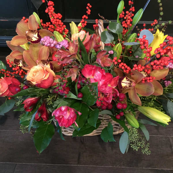 Basket arrangement of roses, orchids, lilies, and red berry stems