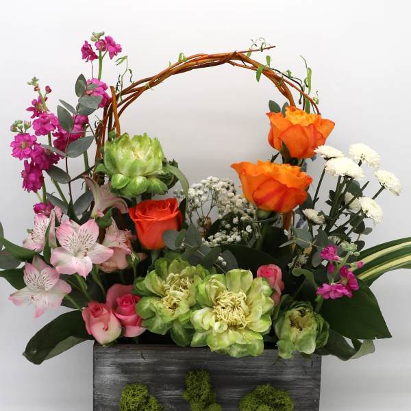 Mixed floral arrangement in a dark wooden box with an arched twig handle