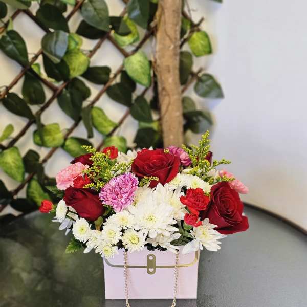 Mixed bouquet of red roses, white daisies, and pink carnations in a pink box