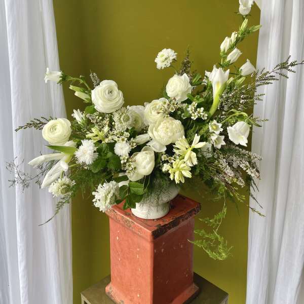 White floral arrangement in a white vase on a pedestal