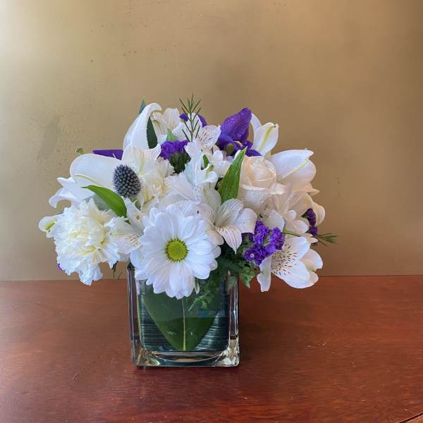 White and purple mixed flower arrangement in a square glass vase