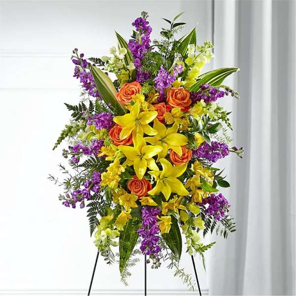 Tall floral spray with yellow lilies, orange roses, and purple blooms on a stand