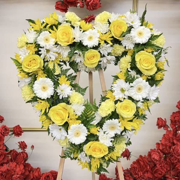 Heart-shaped floral wreath with yellow roses and white daisies on an easel