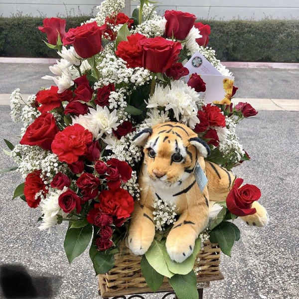 Basket arrangement of red roses, white daisies, and a plush tiger