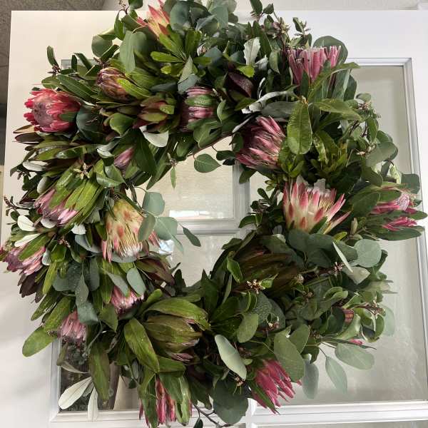 Large wreath with pink protea and mixed greenery on a white door