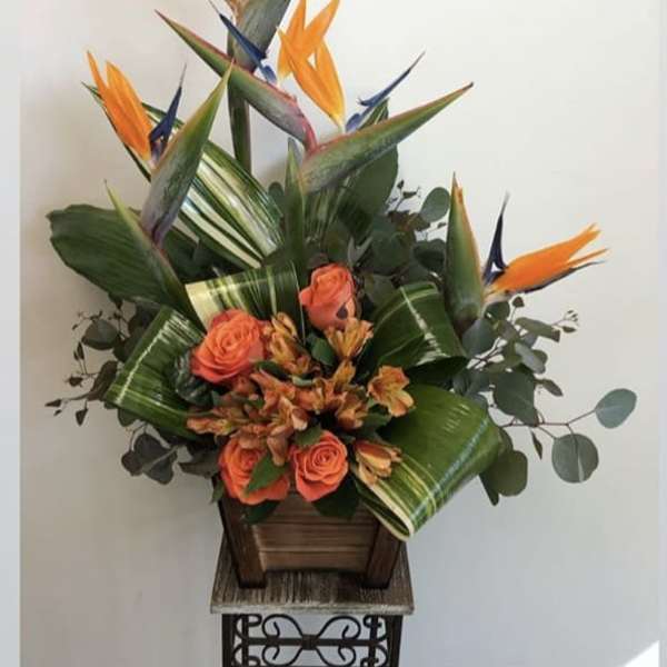 Tropical arrangement with orange birds of paradise and coral roses in a wooden container