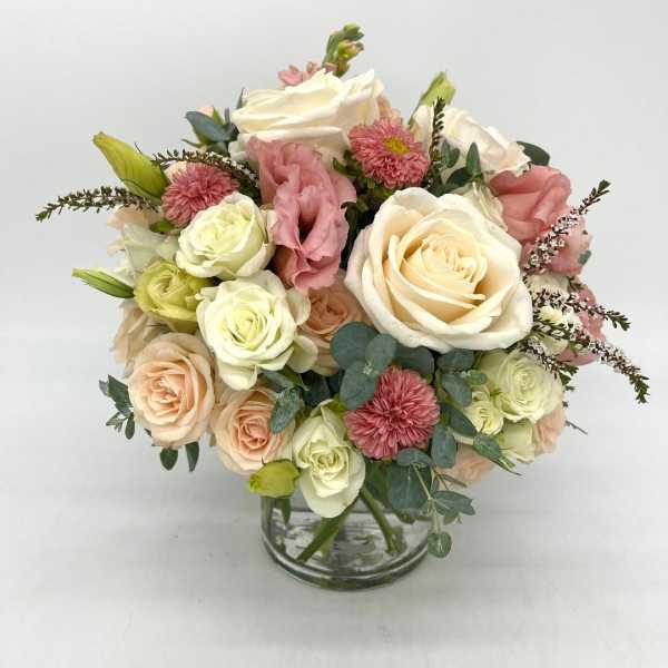 Round arrangement of white and peach roses with pink blooms in a clear glass vase