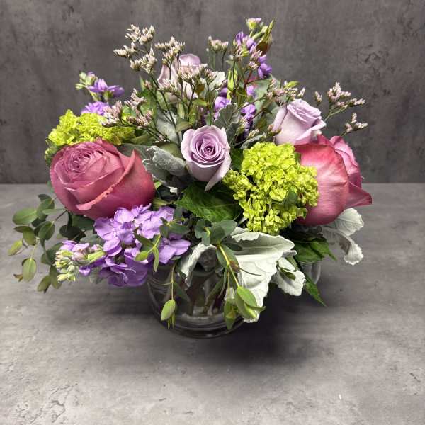 Pink and lavender roses arranged in a glass vase with purple blooms