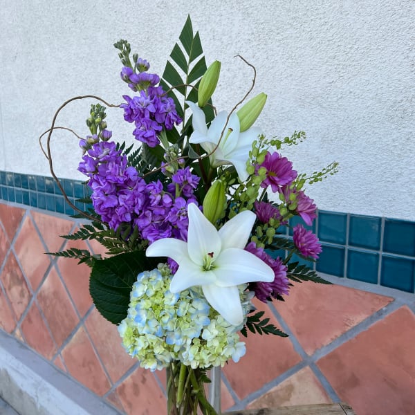 Purple flowers and white lilies arranged in a clear glass vase