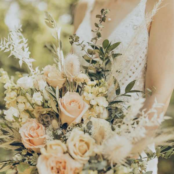 Bride holding a bouquet of peach and cream roses with airy dried accents
