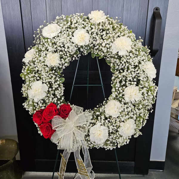 White floral wreath with red roses and a sheer bow on a stand