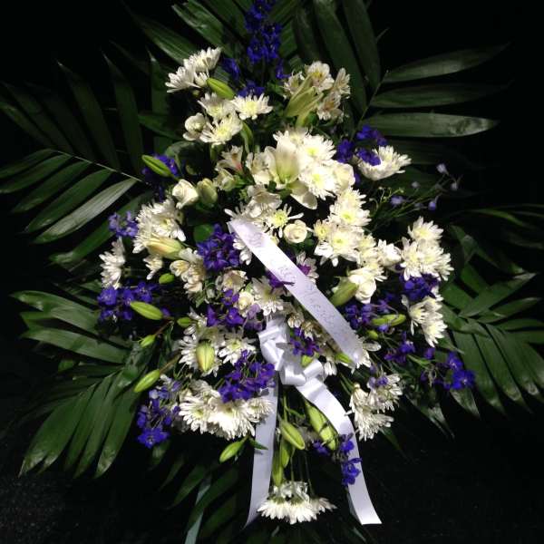 White and purple floral standing spray with ribbon on dark palm leaves