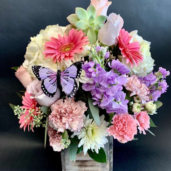 Mixed pink and purple bouquet in a wooden box with a butterfly decoration