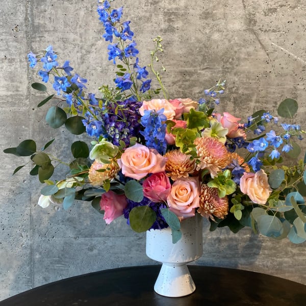 Mixed bouquet in a white pedestal vase with blue and pink flowers