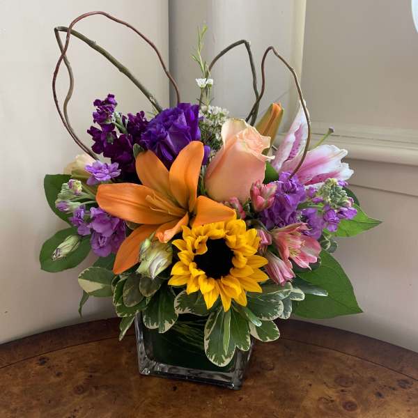 Colorful bouquet with orange lily, sunflower, and pink rose in a glass vase