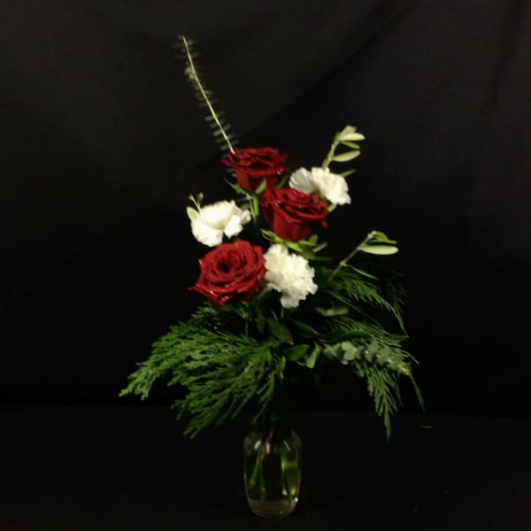 Red and white roses in a clear glass vase with greenery