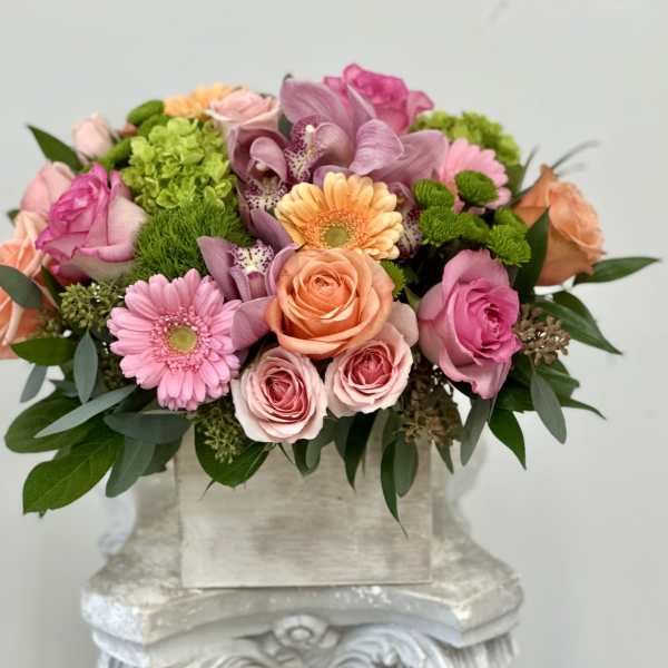 Low arrangement of pink and peach roses, gerbera daisies, orchids and mums in a rustic box vase