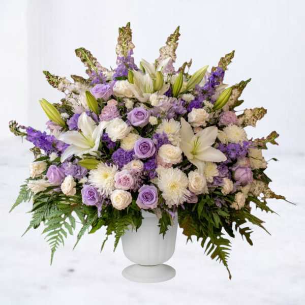 Large lavender and white flower arrangement in a white pedestal urn