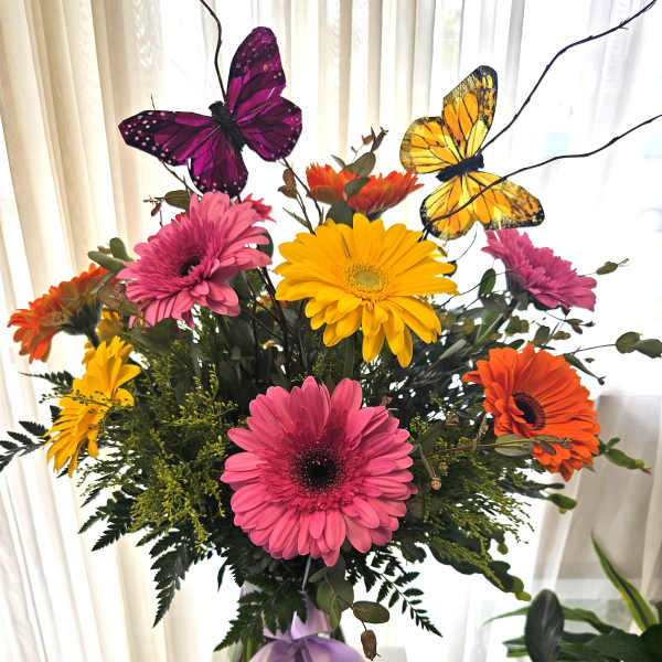 Bouquet of colorful gerbera daisies in a glass vase with butterfly picks